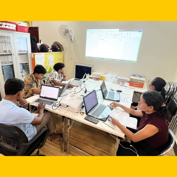 TukTuk staff and volunteers work on laptops in the office while a document is projected on the wall