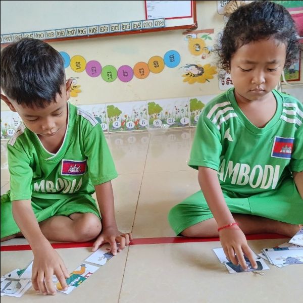 Two children in green shirts sit on the floor and arrange picture cards in a row