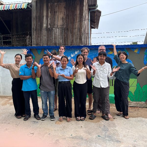 TukTuk staff and volunteers wave and pose together in front of a painted mural wall