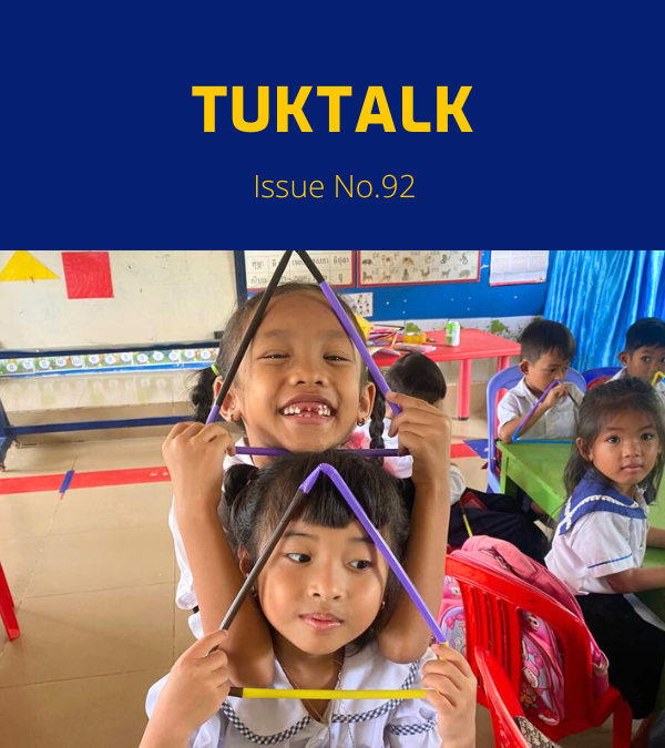Two preschool girls smile and hold triangle shapes made from coloured sticks in a classroom