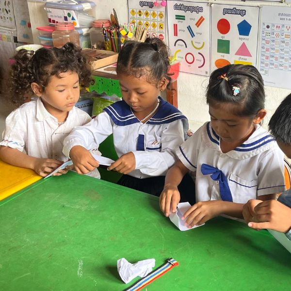 Three girls fold paper at a green classroom table