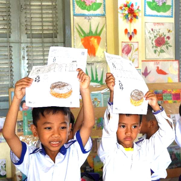 Two boys hold worksheets with a cake picture above their heads in class
