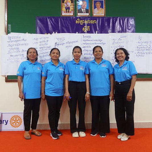 Five teachers in blue shirts pose together in front of a workshop banner