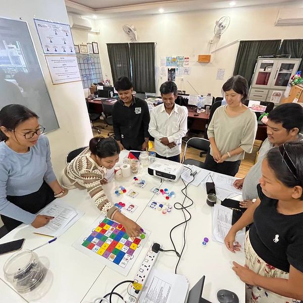 TukTuk staff and volunteers gather around a table to play a colourful board game in the office