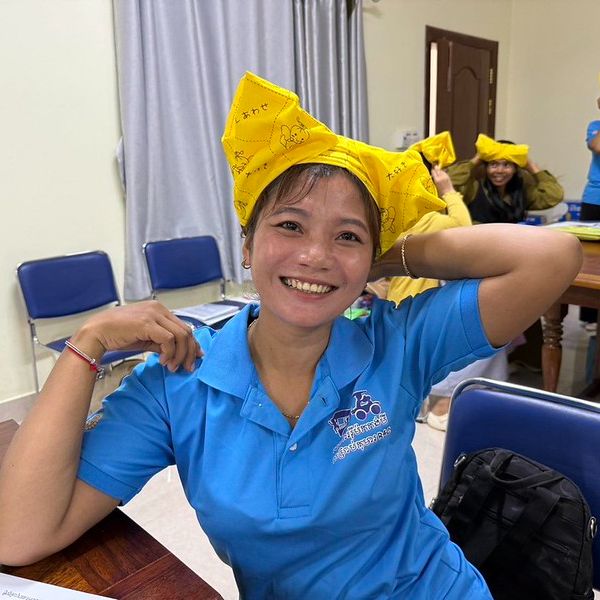 A smiling teacher wears a yellow paper hat she made at the workshop