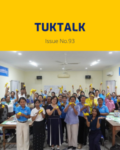 Teachers at the final workshop cheer and hold up yellow paper crafts in a classroom