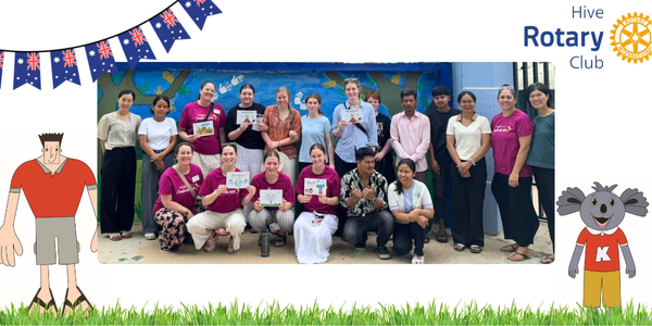 Group photo of HIVE Rotary Club visitors and TukTuk staff holding picture books, framed with Australian flags and a koala