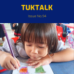 A preschool girl rests her chin on her arm and colours a worksheet with a purple pencil