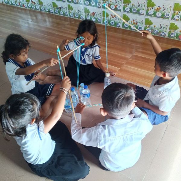 Children sit on the floor and play with sticks and string around water bottles
