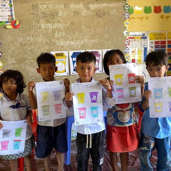 Children hold up their coloured recycling bin worksheets in the classroom