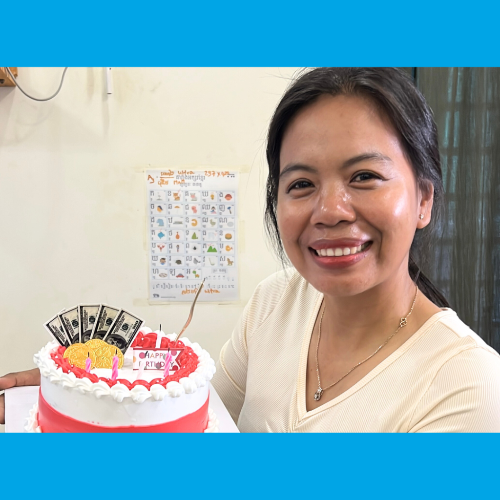 A smiling TukTuk staff member holds a birthday cake decorated with play money
