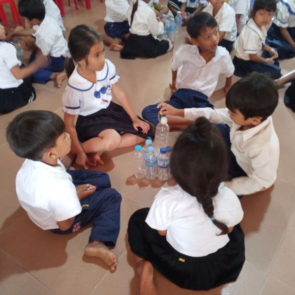 Children sit in a circle on the classroom floor playing a game with water bottles