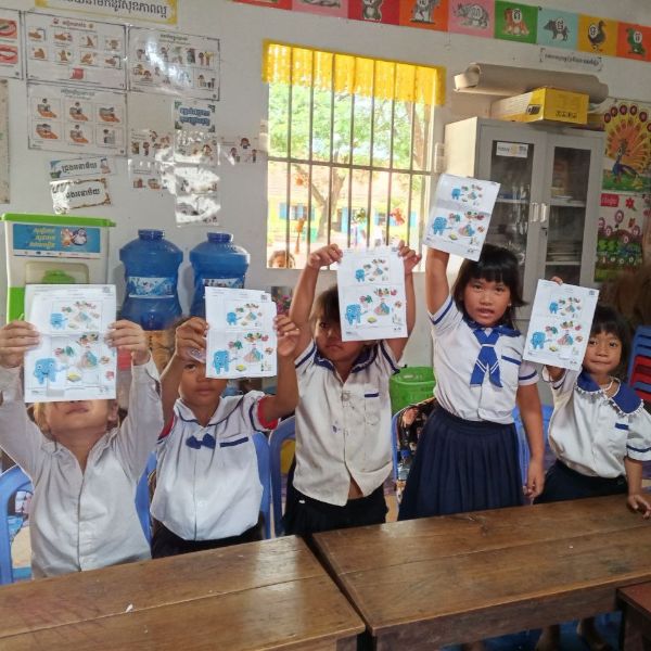 Pupils in school uniform hold up their completed worksheets in a classroom