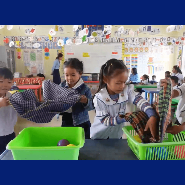 Children in a classroom pick up checked scarves and place them into green plastic baskets