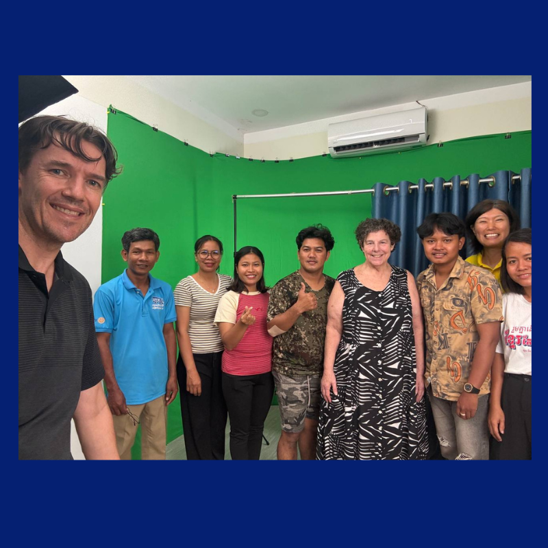 A man takes a group selfie with TukTuk staff and visitors in front of a green screen in the studio