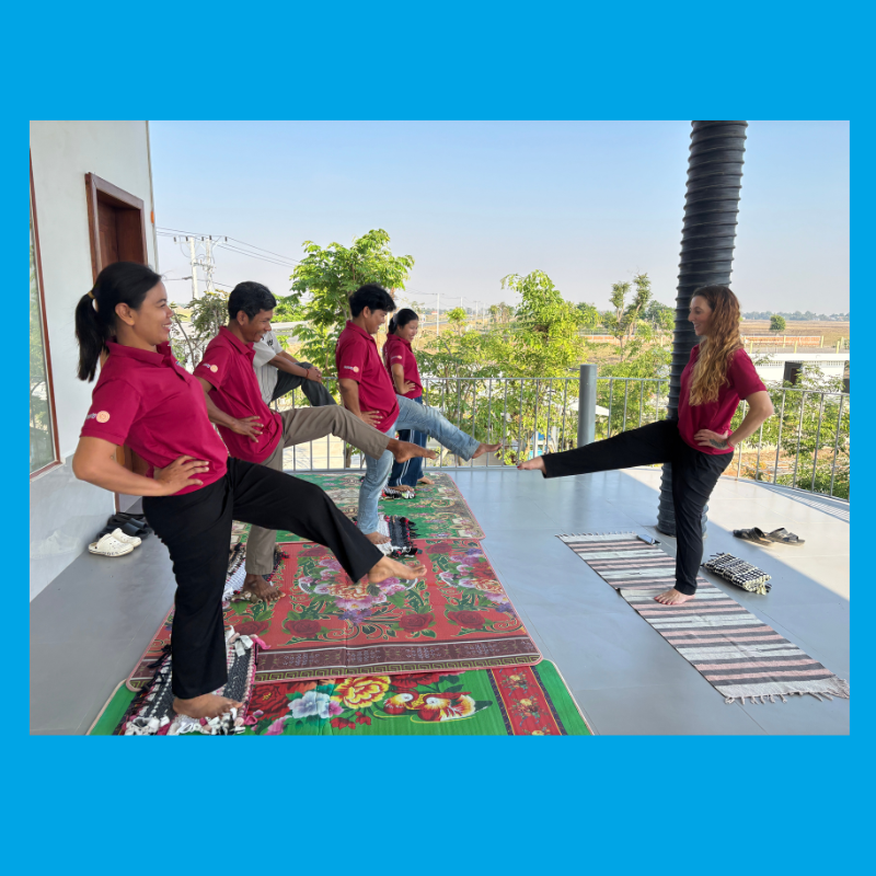 TukTuk staff in maroon shirts stretch their legs during a wellbeing session on a covered balcony
